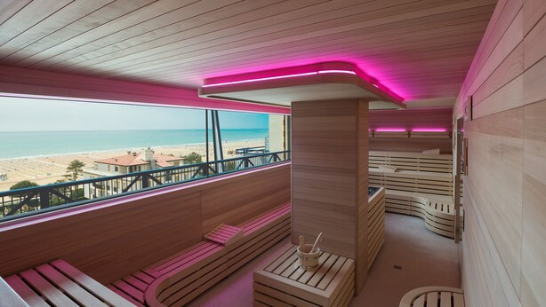 A wooden interior with benches and a sauna area, overlooking a beach.