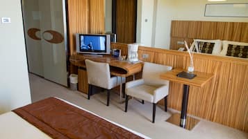 Une chambre d’hôtel comprenant un lit, un bureau avec un ordinateur, deux chaises, une machine à café et une petite table avec une lampe.