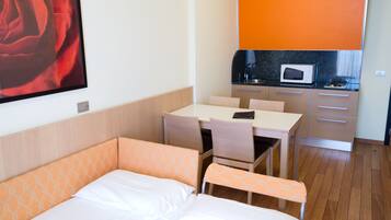 Ein Hotelzimmer mit einem Bett, einem kleinen Esstisch, einer Küchenzeile inklusive Mikrowelle und einem großen, gerahmten Bild an der Wand.