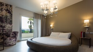 A modern bedroom with a large bed, a chandelier, a nightstand, and a view of the outdoors.