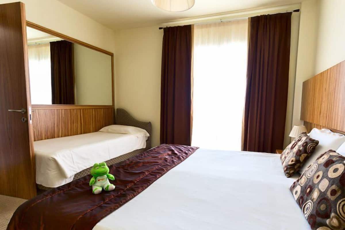 A hotel room with a large bed, a smaller bed, a mirror, and two windows with curtains.