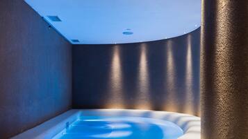 A modern spa room with a hot tub, steps leading up to it, and a ceiling with recessed lighting.