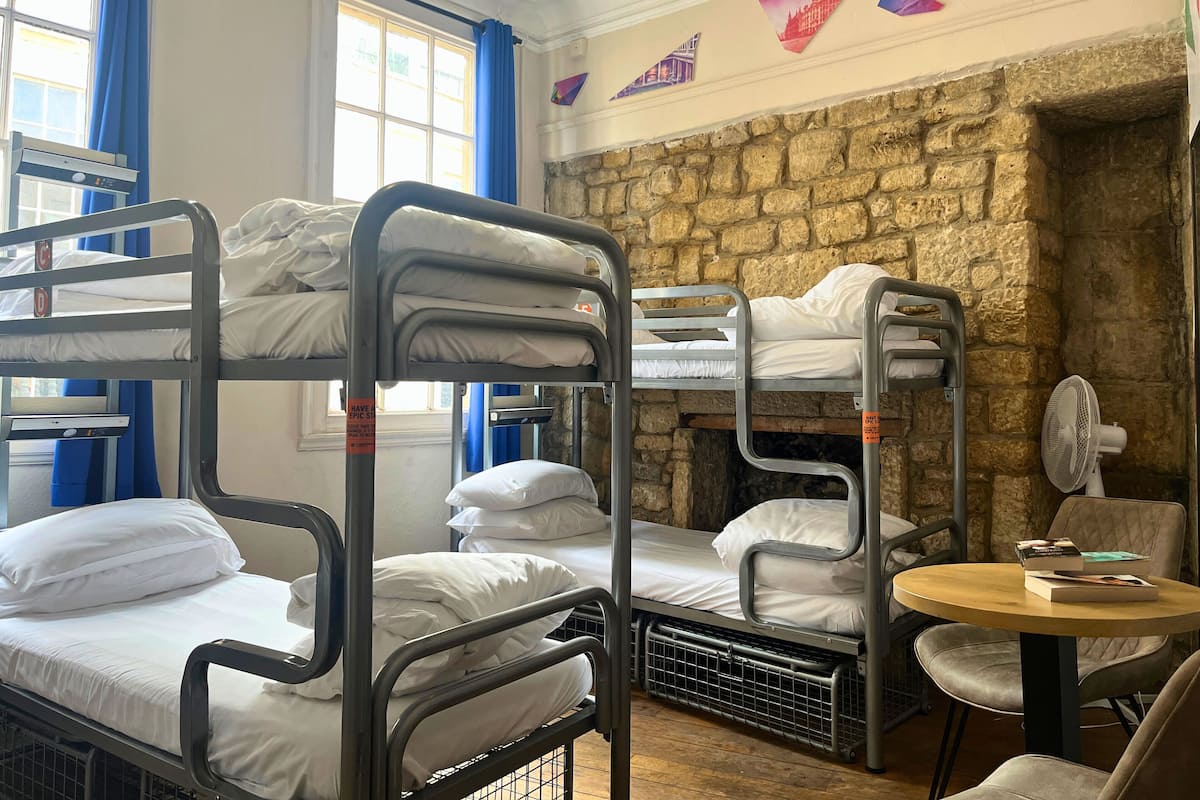 A bunk bed room with a stone wall, a fan, and a table with books.