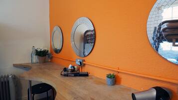 Un salón de belleza con un mostrador de madera, dos espejos grandes, un secador de pelo y un radiador.