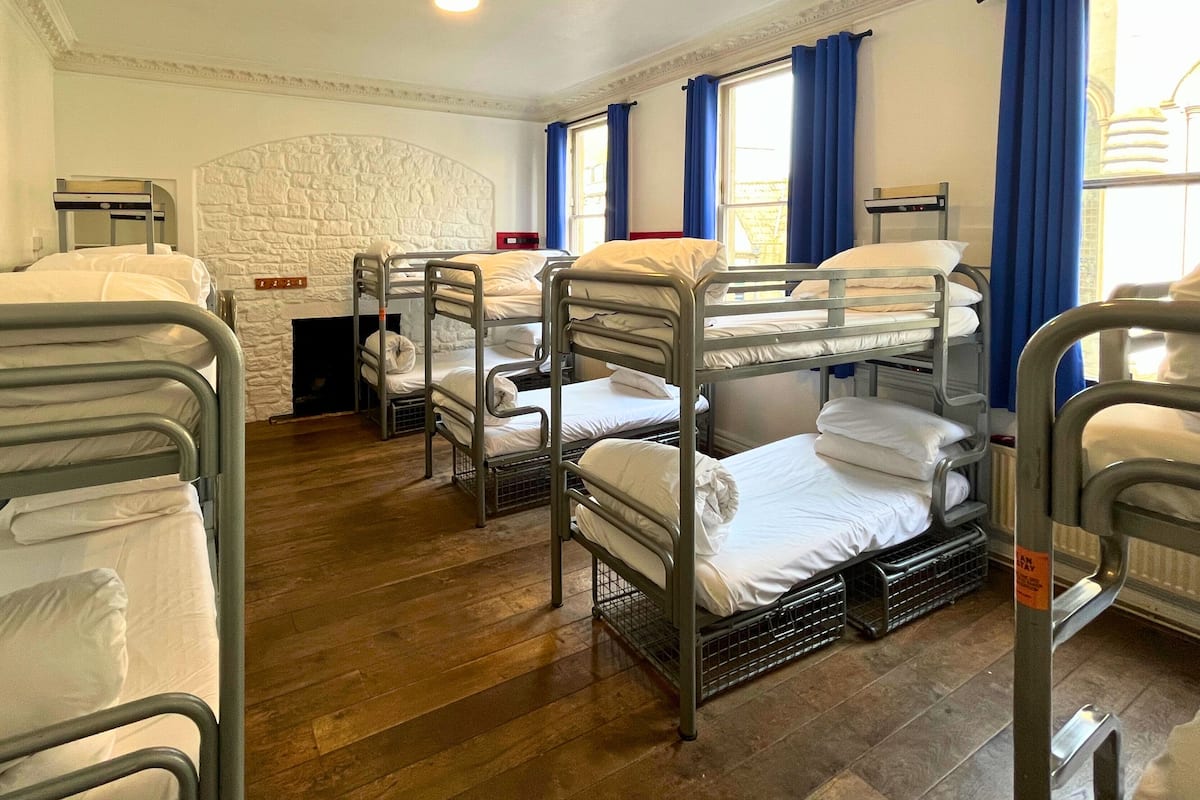 A hotel room with bunk beds, a fireplace, and large windows with blue curtains.