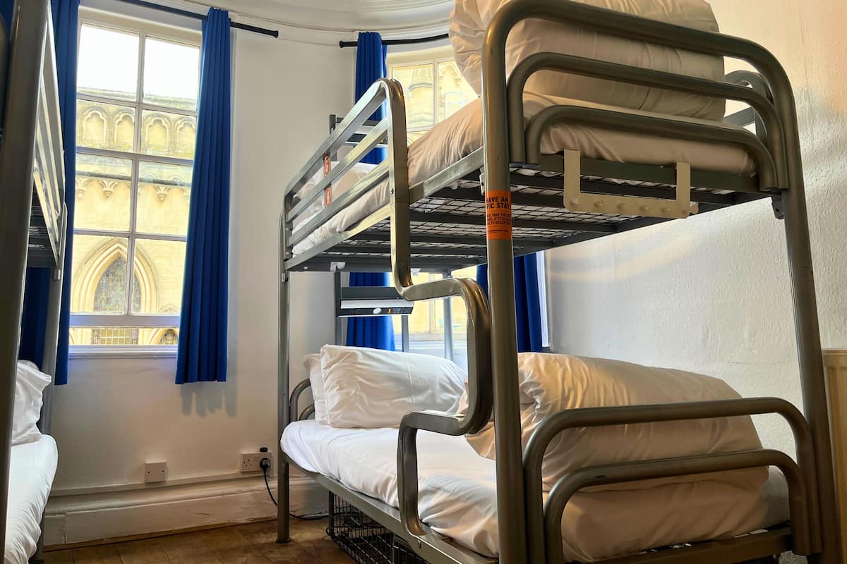 A bunk bed room with a window, blue curtains, and a view of a building with arches.