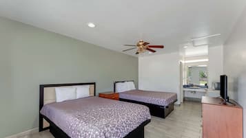 Une chambre d’hôtel avec deux lits, un ventilateur de plafond, un bureau avec une télévision et une salle de bain visible au fond.