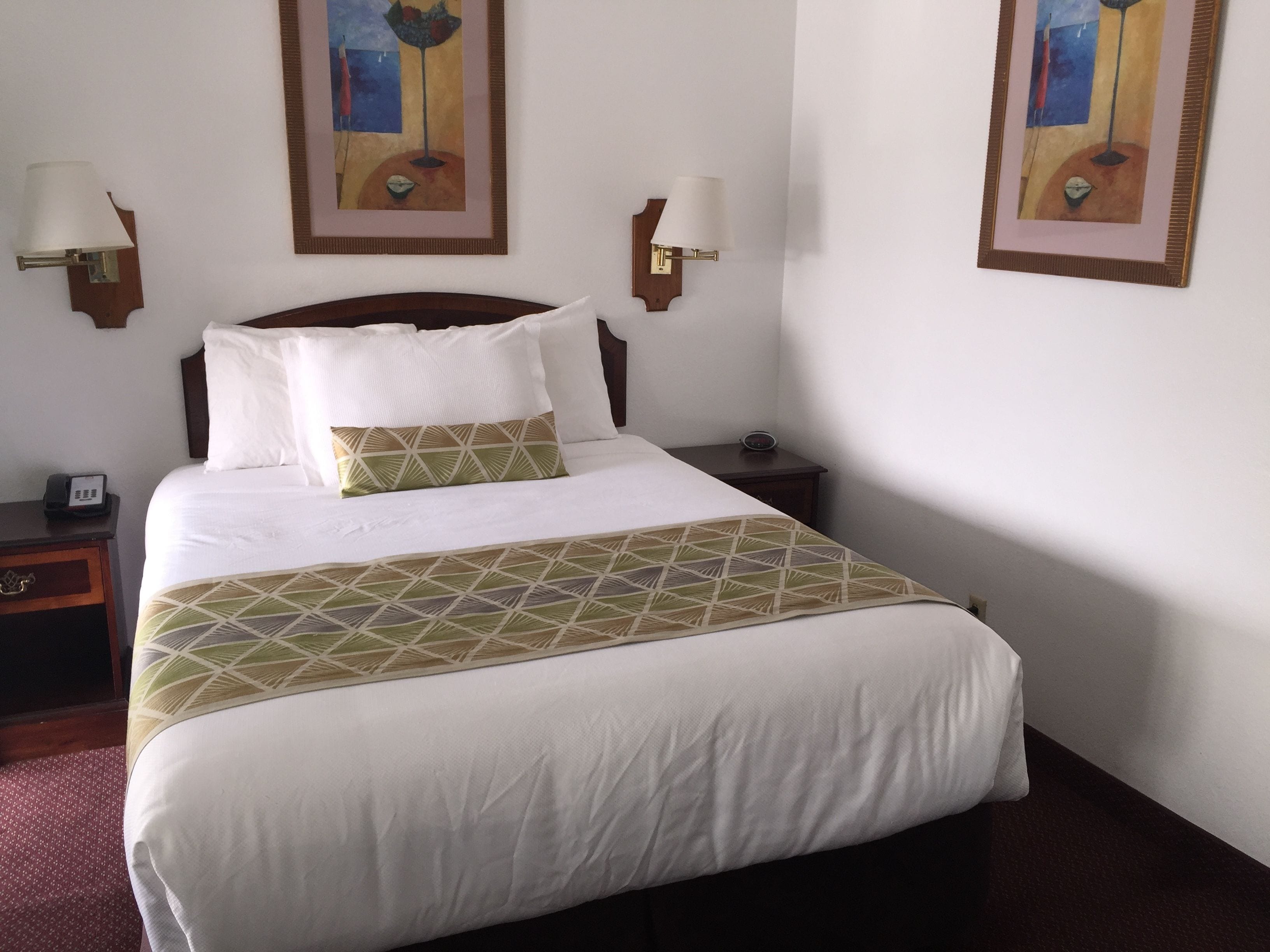 Quarto de hotel com uma cama grande, duas mesas de cabeceira, um criado-mudo e duas luminárias fixadas na parede.
