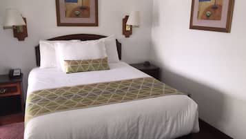 Quarto de hotel com uma cama grande, duas mesas de cabeceira, um criado-mudo e duas luminárias fixadas na parede.