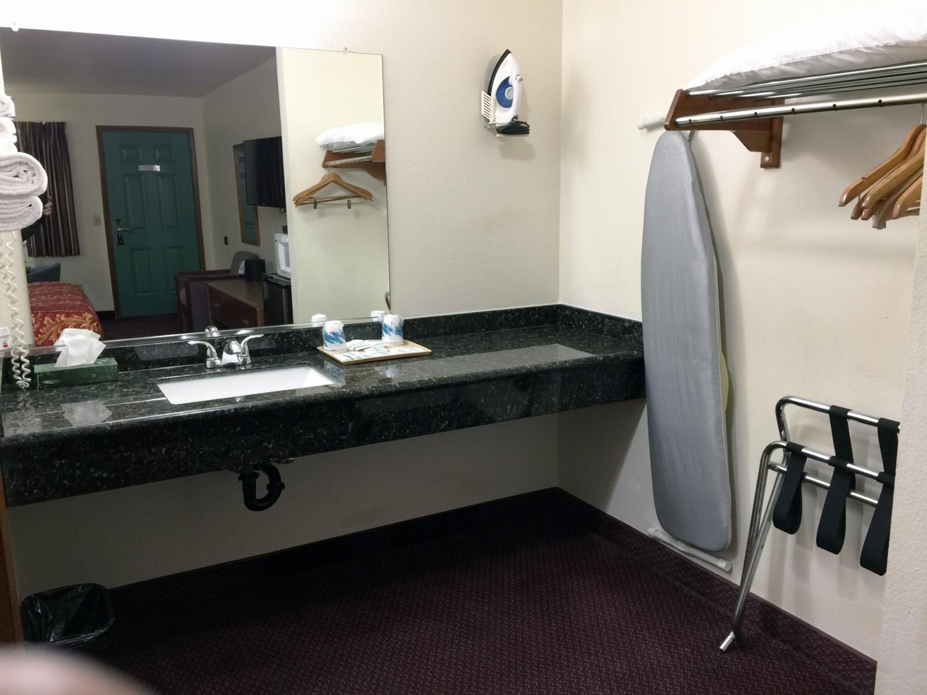 Une salle de bain d’hôtel équipée d’un lavabo, d’un miroir, d’un porte-vêtements et d’une planche à repasser.