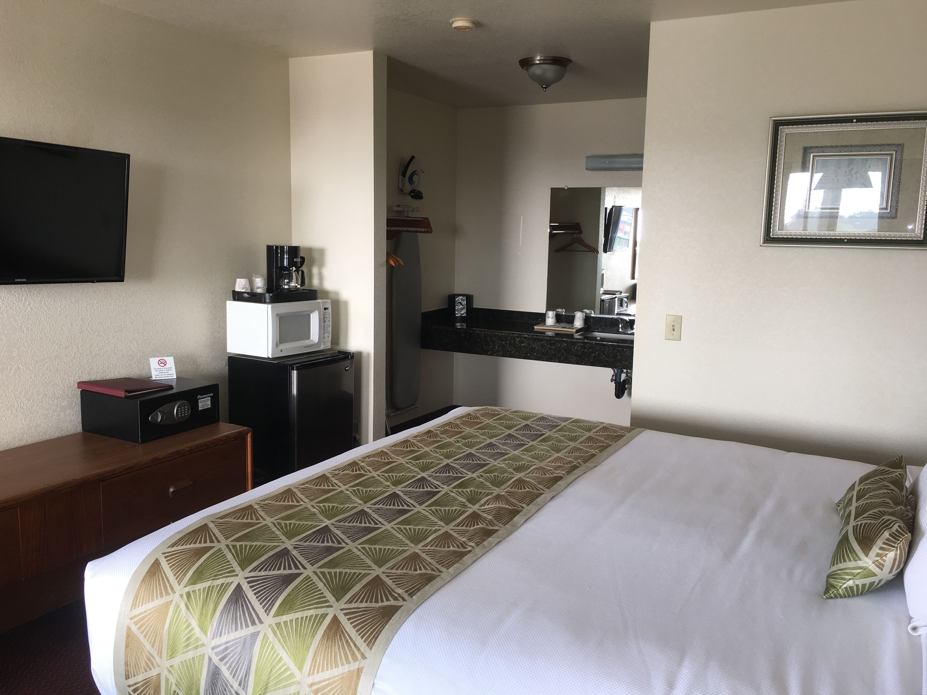 A hotel room with a bed, a desk with a computer, a microwave, and a TV.