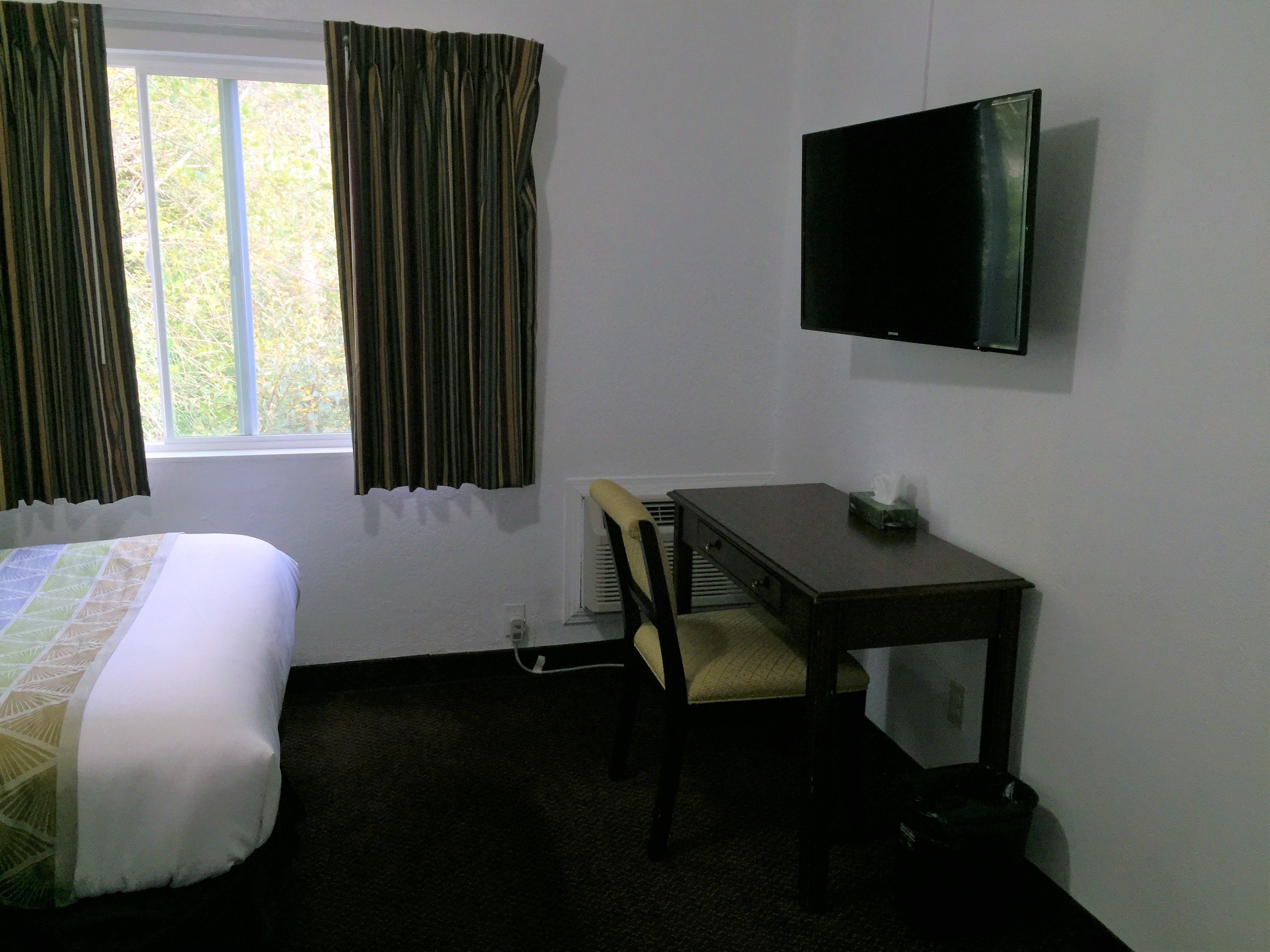 A hotel room with a bed, a desk with a chair, a television, and a window with curtains.