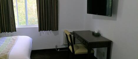 A hotel room with a bed, a desk with a chair, a television, and a window with curtains.