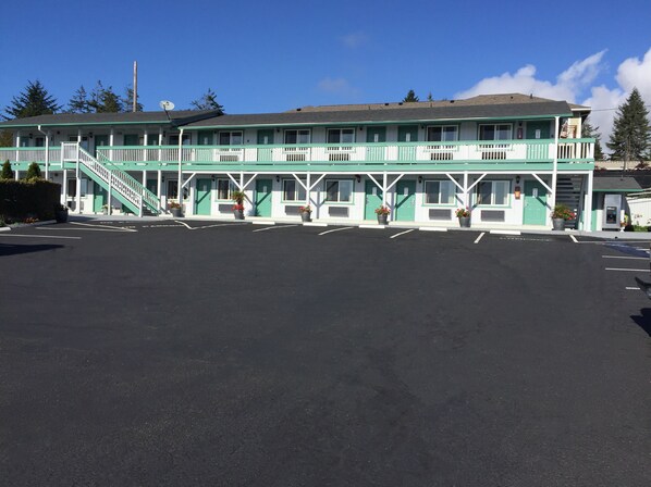 A motel with a green and white exterior, a covered parking area, and a staircase leading to the entrance.