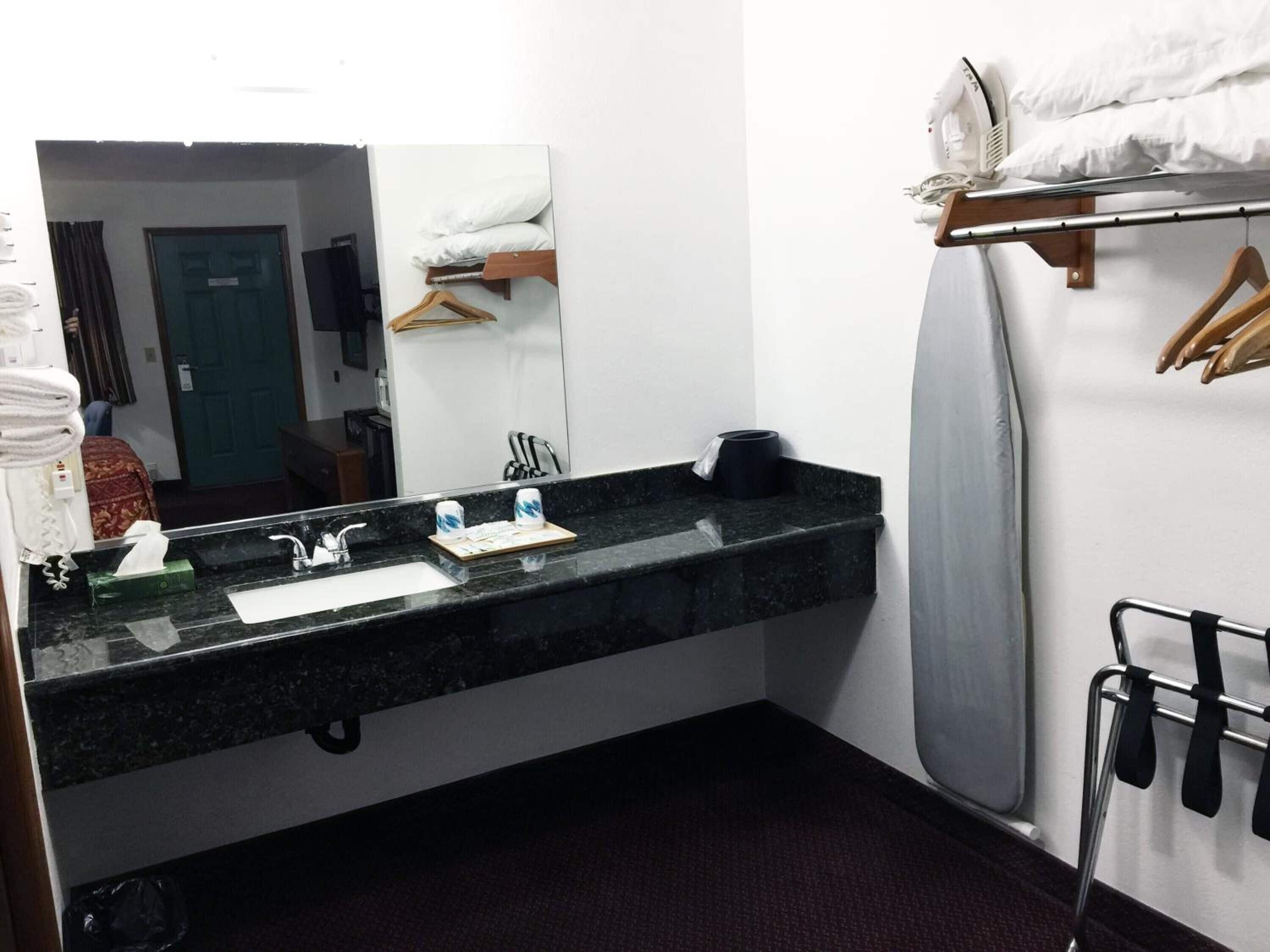 A hotel bathroom with a black granite sink, a mirror, a towel rack, and a shower area.