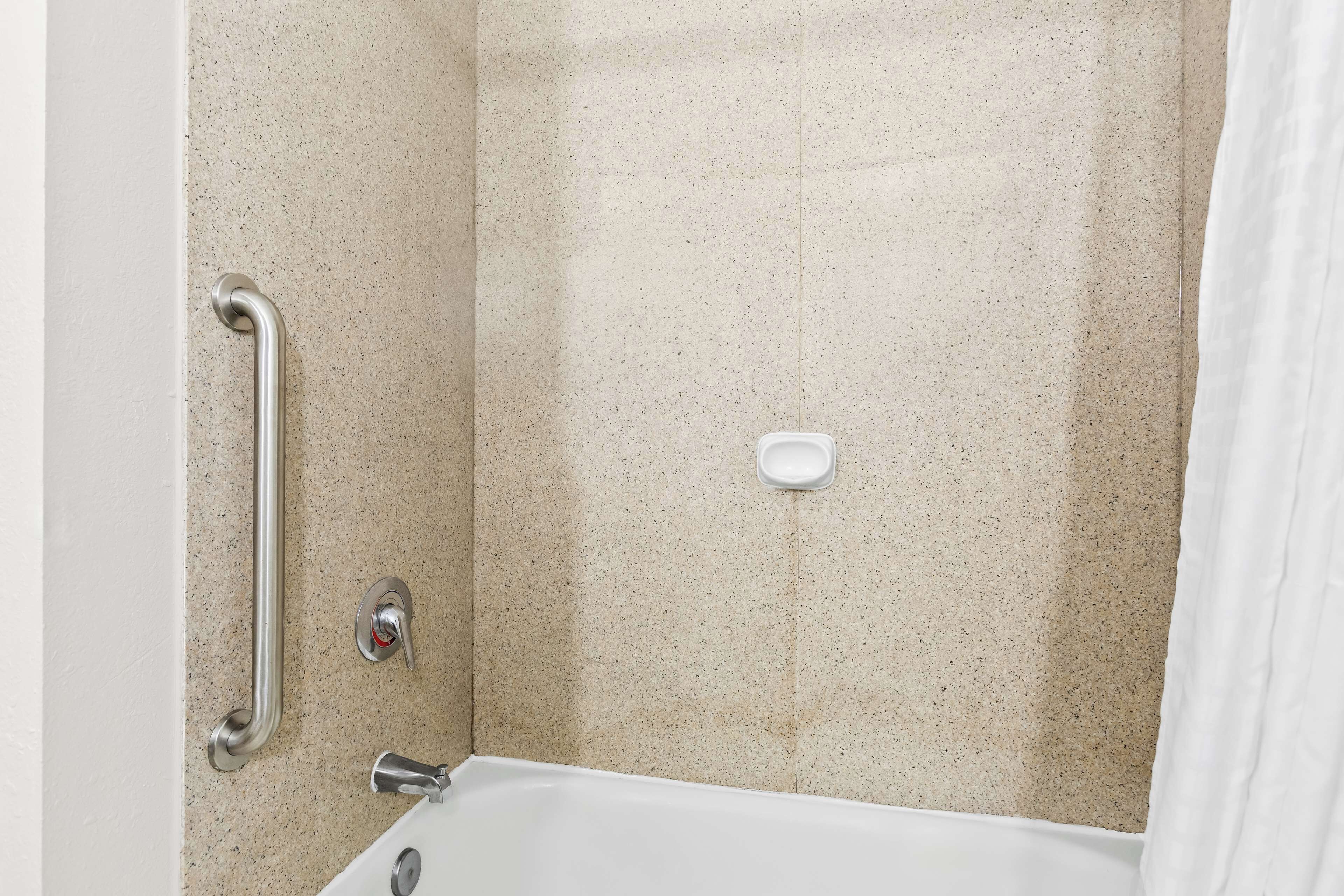 A bathroom with a shower, grab bar, and a soap dish.
