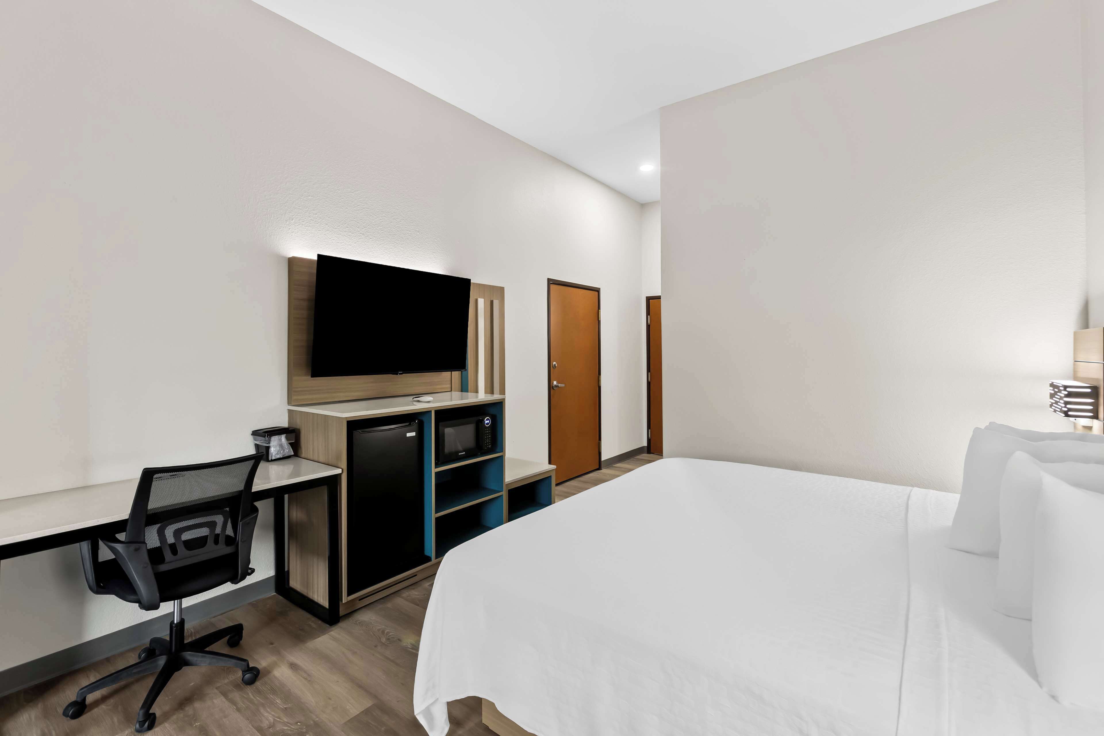 A hotel room with a bed, a desk with a computer, a TV, a microwave, and a wardrobe.