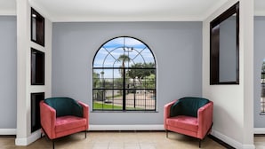 Ein Zimmer mit zwei rosafarbenen Sesseln, einem großen Bogenfenster mit Blick auf einen Park und einem Fliesenboden.