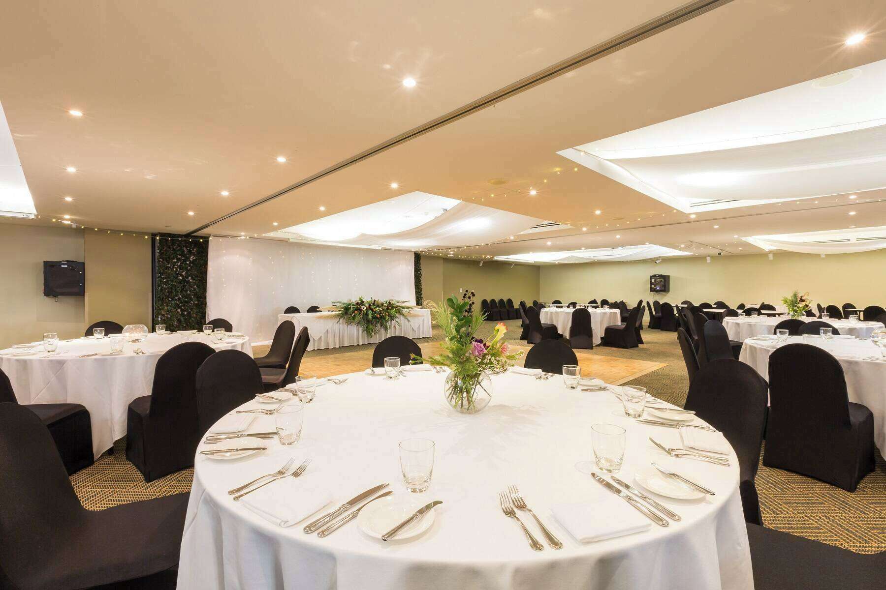 A banquet hall with round tables set for dining, featuring white tablecloths and gold cutlery.