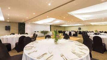 A banquet hall with round tables set for dining, featuring white tablecloths and gold cutlery.
