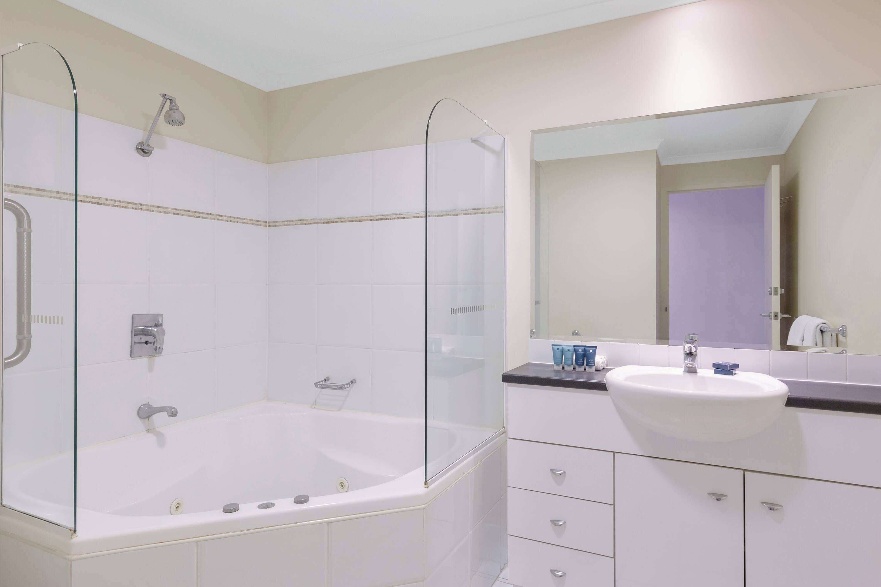 Ein modernes Badezimmer mit einer gläsernen Duschkabine, einer weißen Badewanne und einem Waschtisch mit Waschbecken und Spiegel.
