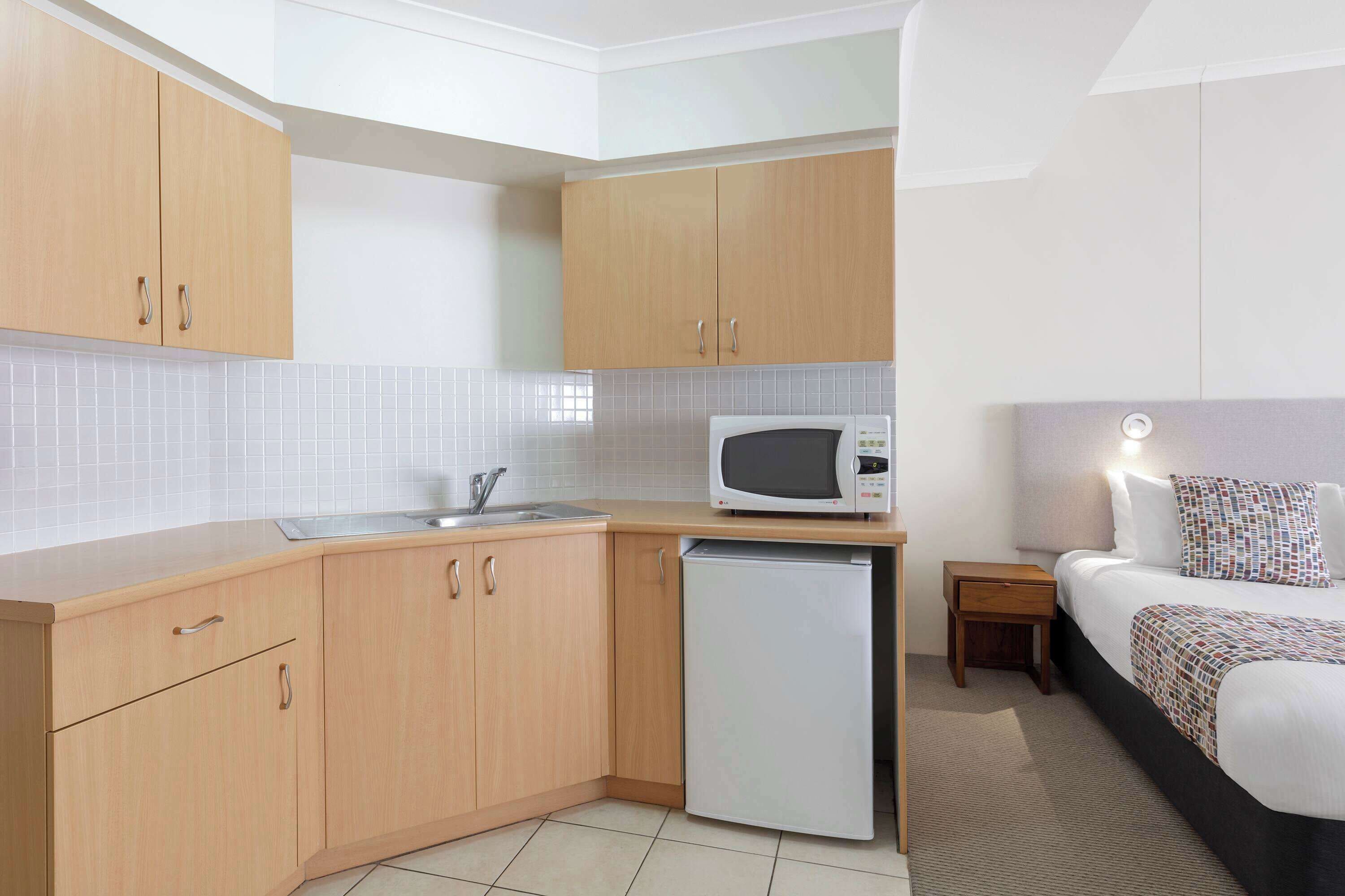 A compact hotel room with a kitchenette, a bed, and a bedside table.