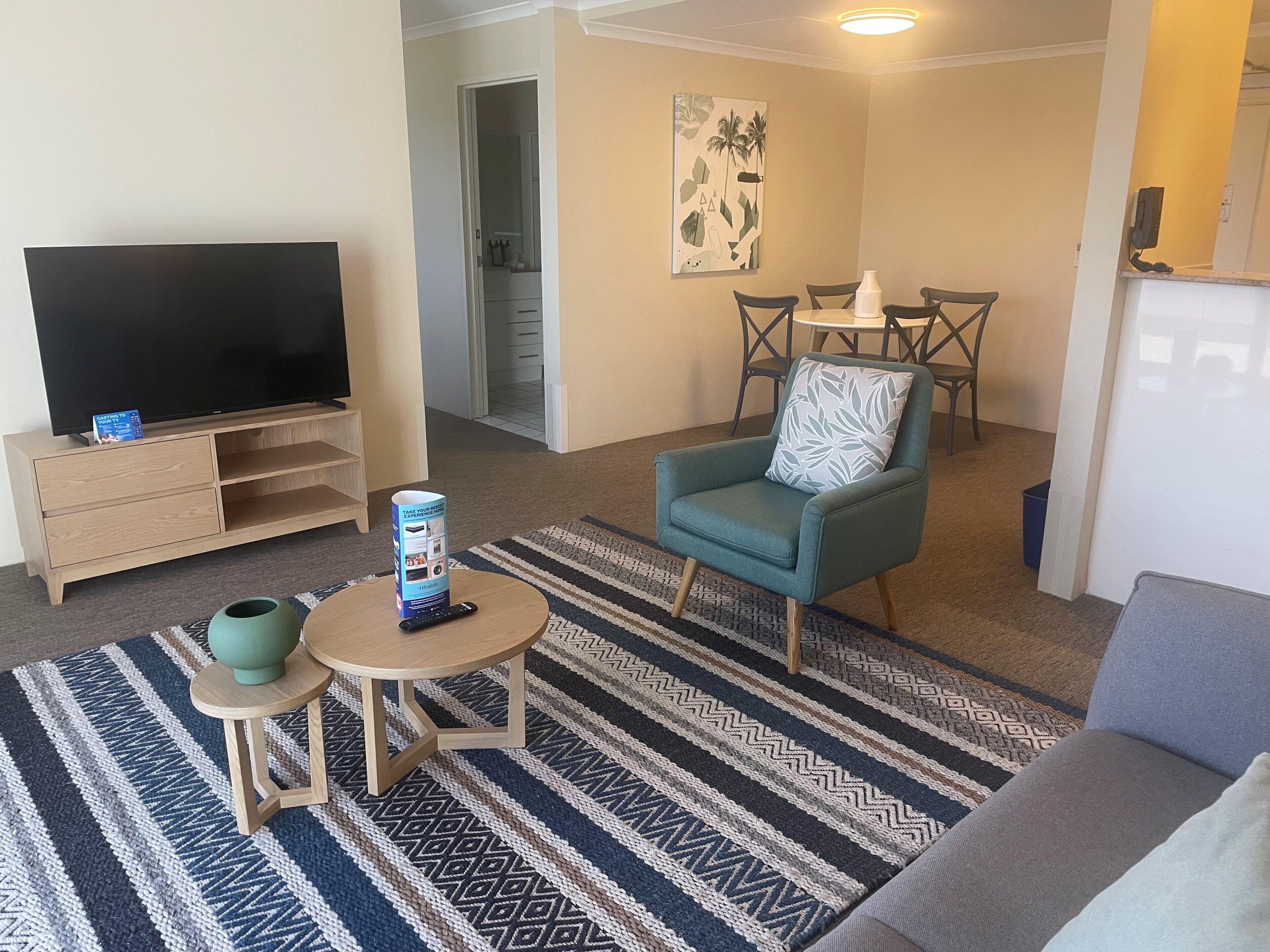 A living room with a TV, a small table, a chair, and a patterned rug.