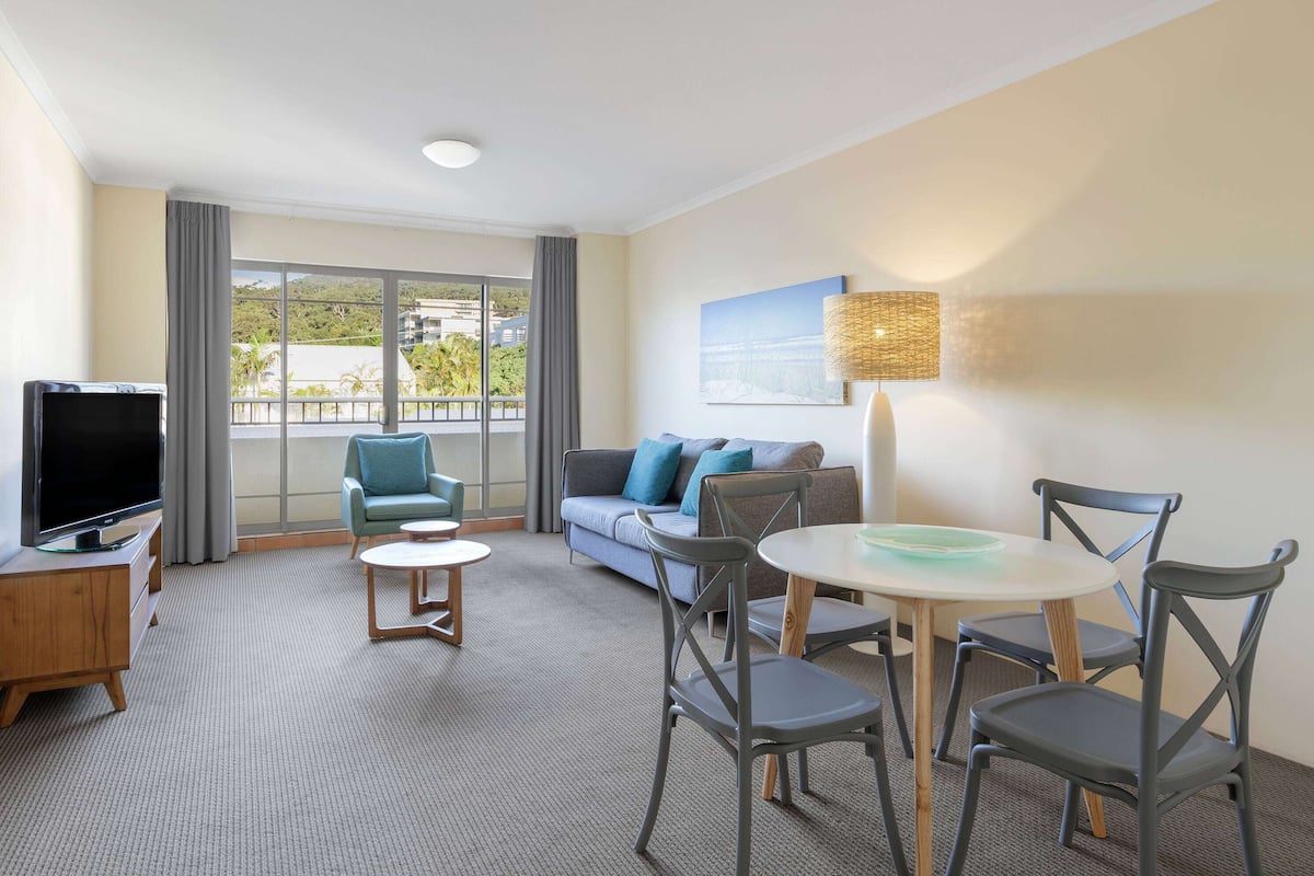 Ein Hotelzimmer mit großem Fenster, einer Couch, einem Fernseher und einem Essbereich mit Stühlen und Tisch.