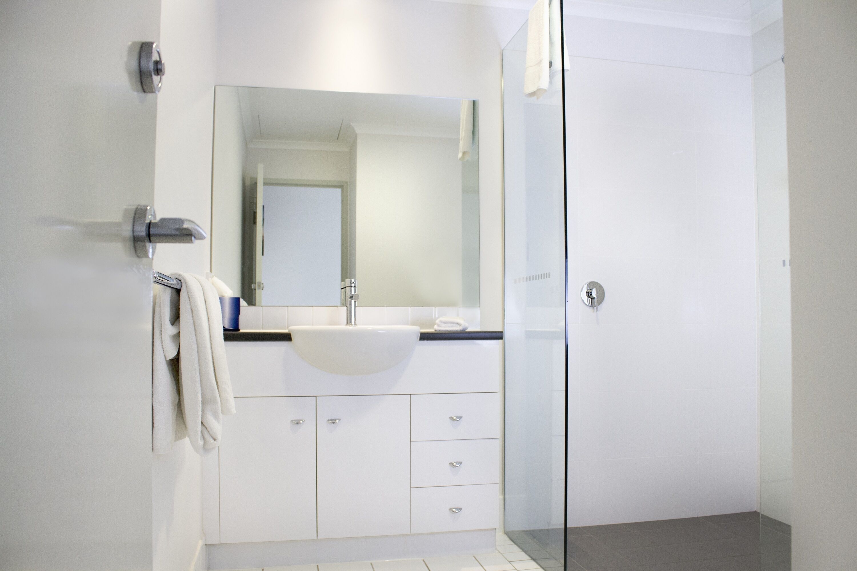 A modern bathroom with a white sink, mirror, and glass shower enclosure.