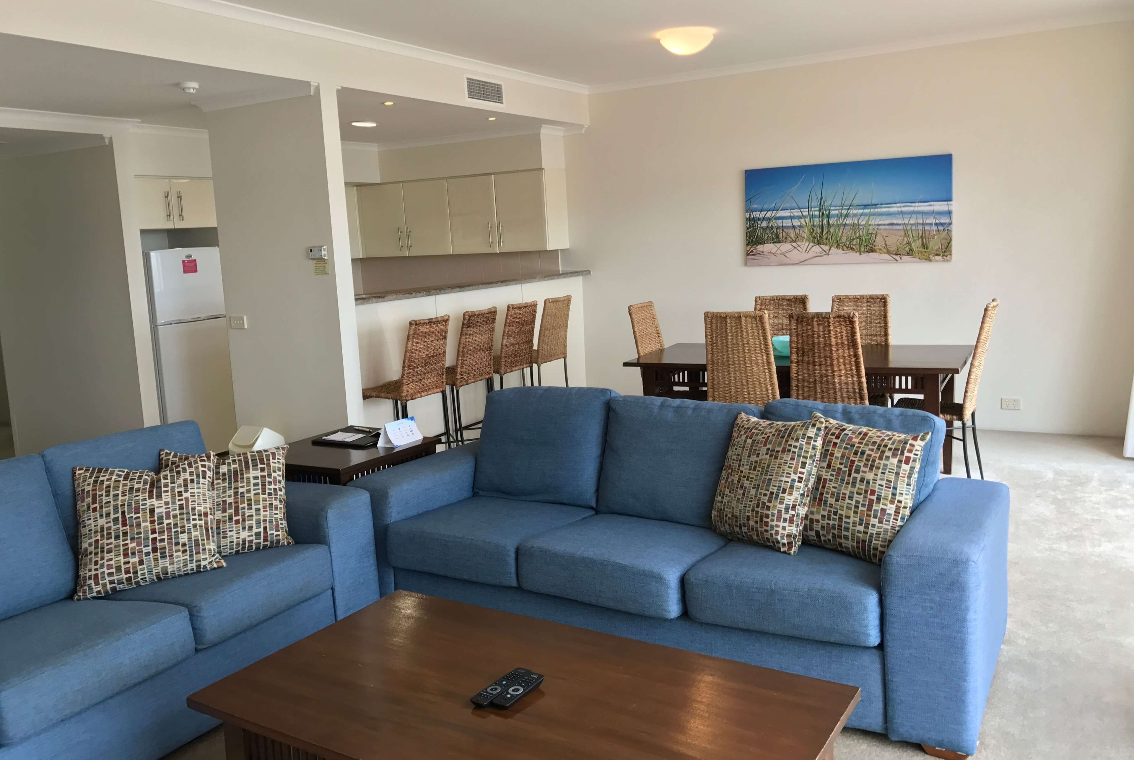 A living room with a blue sofa, a wooden coffee table, and a dining area with wicker chairs and a table.