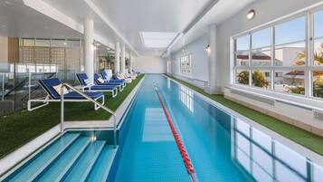 Una piscina interior con azulejos azules, un separador de carril rojo y sillones de descanso a los lados.