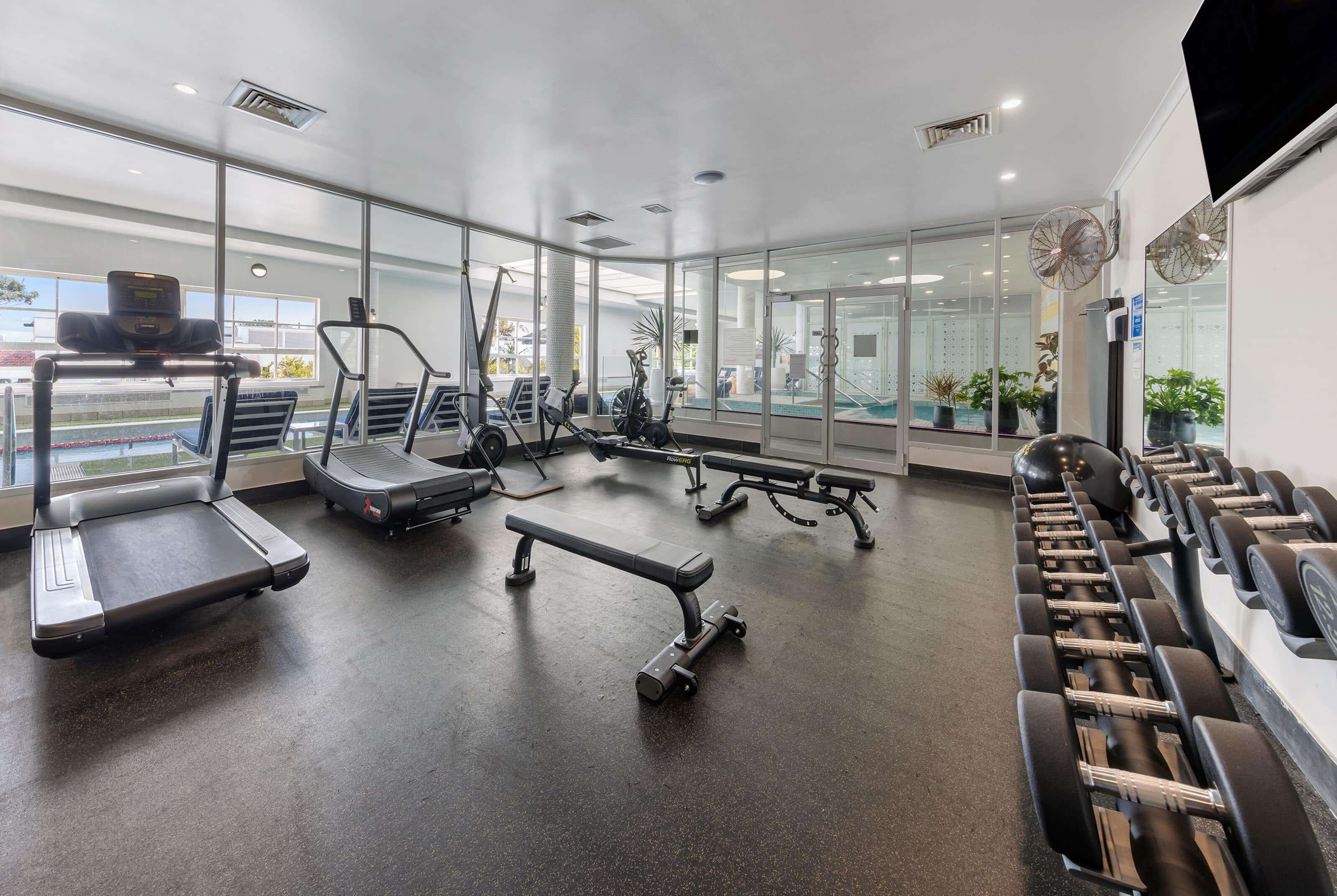 Un gimnasio moderno con cintas de correr, elípticas, bancos y mancuernas.