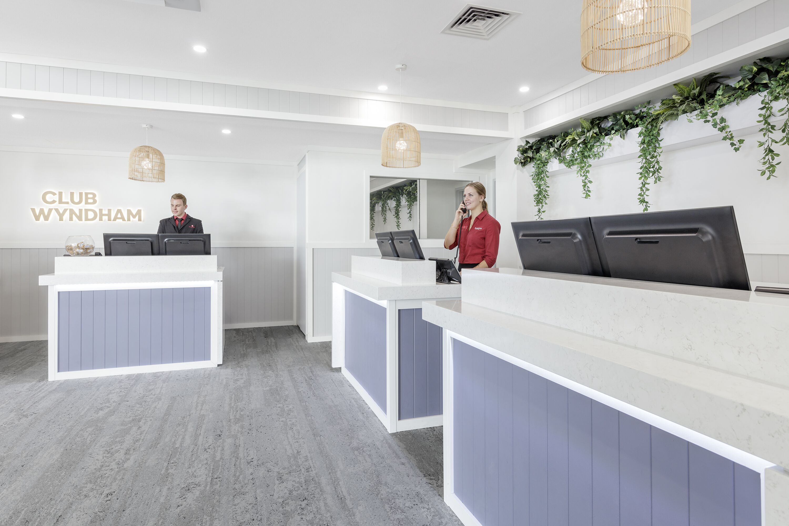 Un espace d’accueil aux couleurs blanc et gris, comprenant un comptoir d’accueil, un guichet et une enseigne fixée au mur sur laquelle on peut lire « CLUB WYNDHAM ».