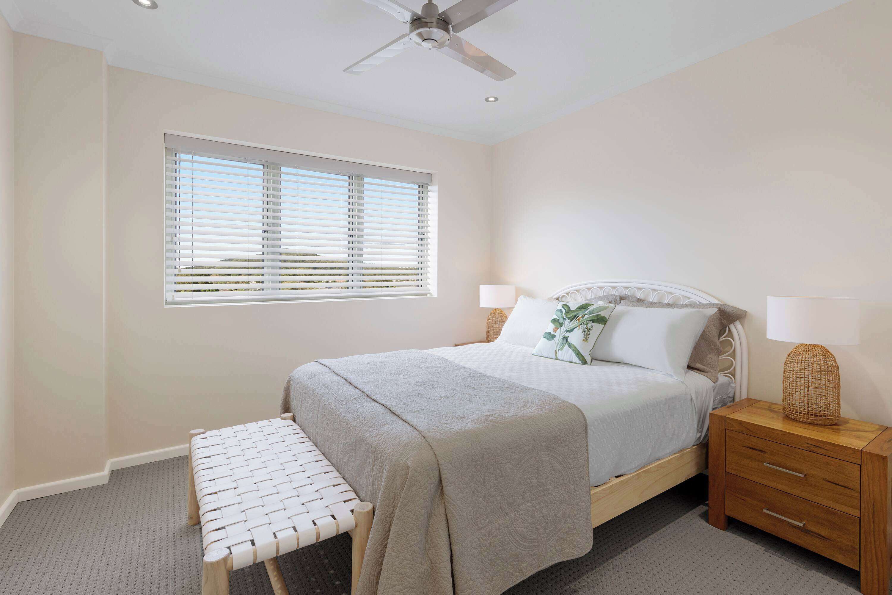 A bedroom with a bed, bedside table, lamp, and window with blinds.