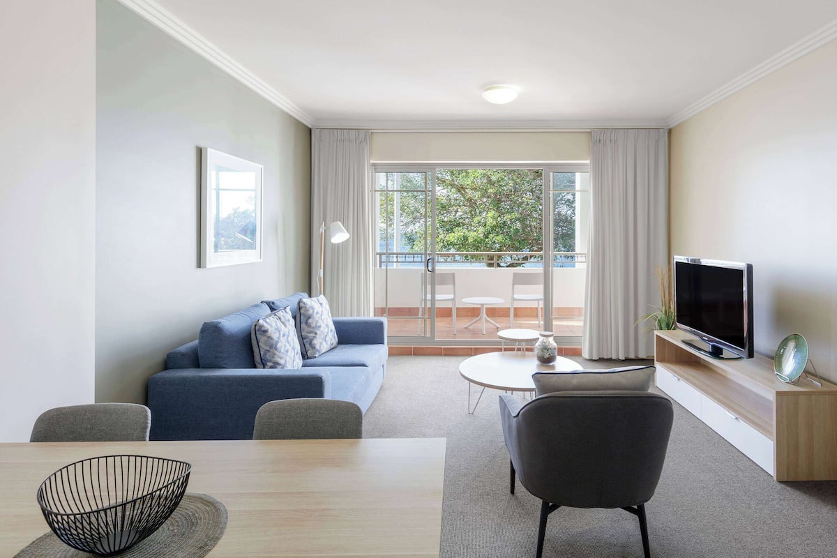 Ein modernes Wohnzimmer mit Sofa, Fernseher, Esstisch und einem Balkon mit Blick.