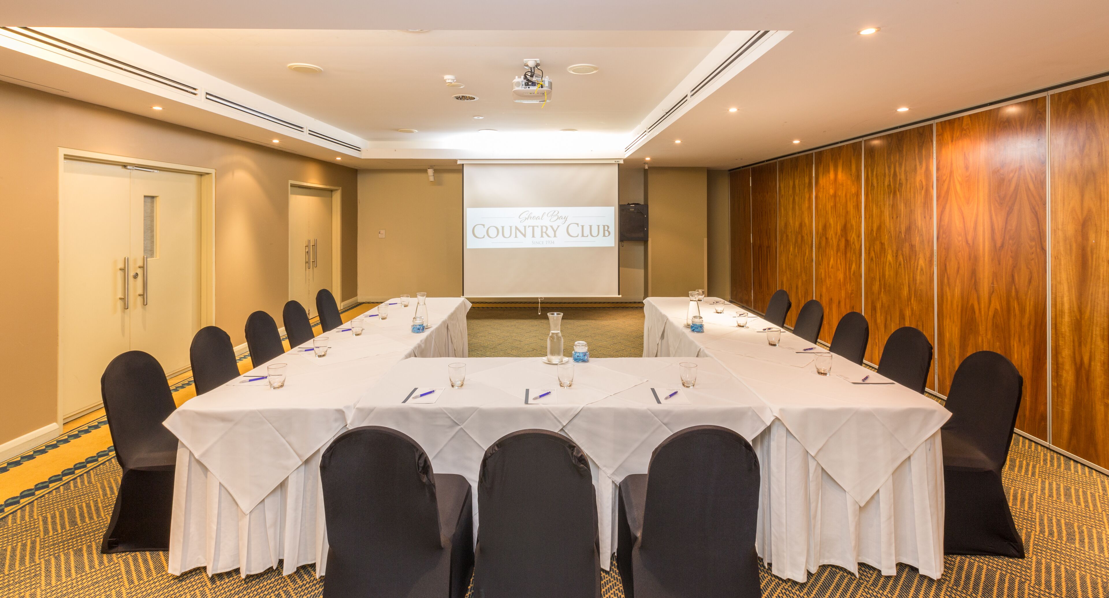Una sala conferenze con un lungo tavolo, sedie e uno schermo che mostra "Great Bay Country Club".