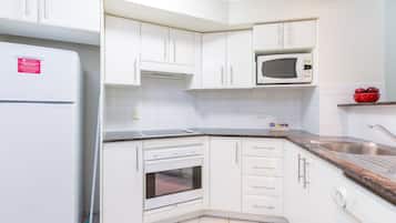 Una cocina con armarios blancos, un microondas, un lavamanos y un tazón rojo sobre la encimera.