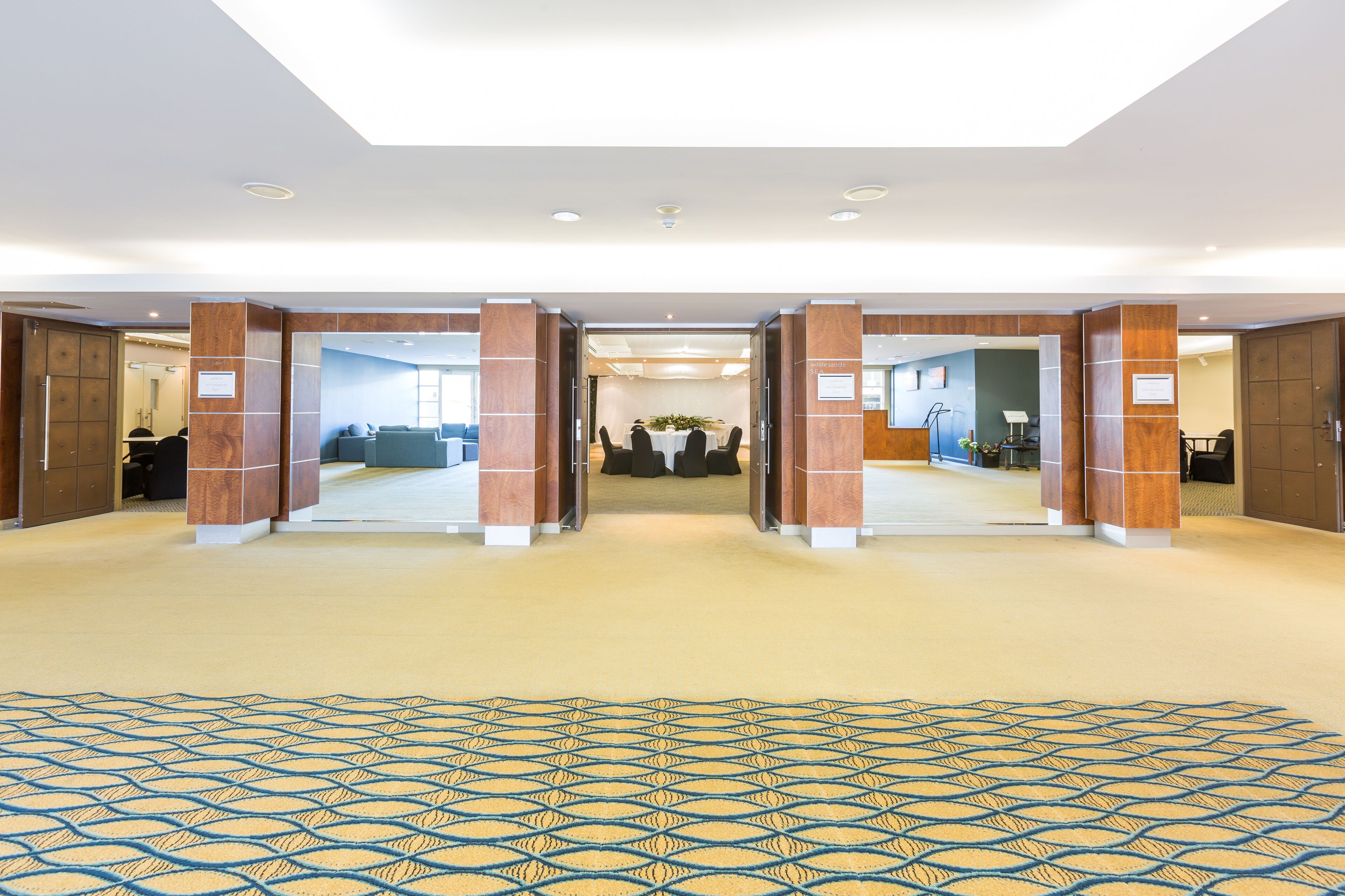 Un hall de hotel con alfombra estampada, pilares de madera y una mesa de recepción.