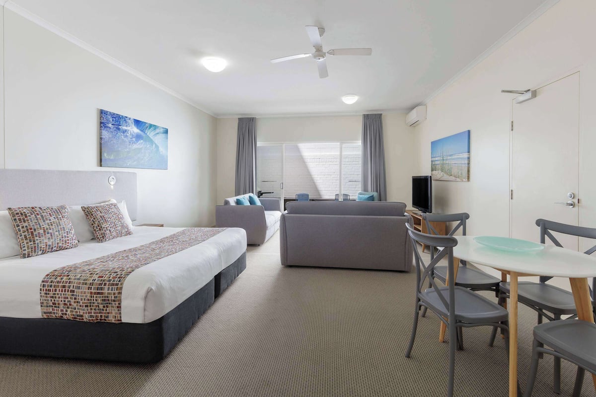 Ein Hotelzimmer mit Bett, Sofa, Esstisch mit Stühlen, Deckenventilator und Fernseher.