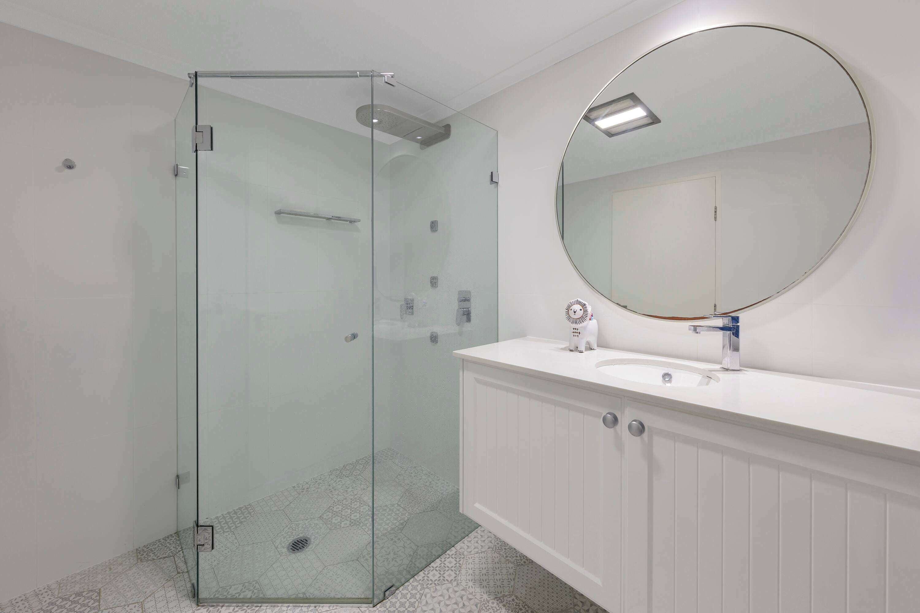 Une salle de bain moderne avec une douche à parois de verre, un miroir rond et un meuble-lavabo blanc.
