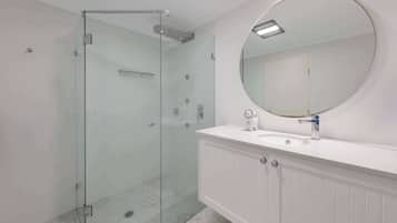 Une salle de bain moderne avec une douche à parois de verre, un miroir rond et un meuble-lavabo blanc.