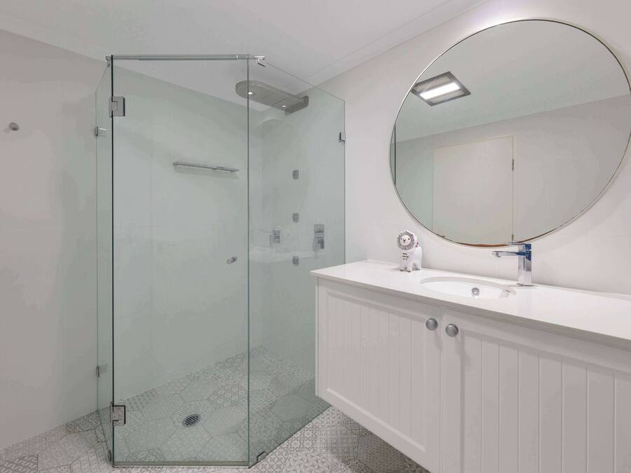 Une salle de bain moderne avec une douche à parois de verre, un miroir rond et un meuble-lavabo blanc.