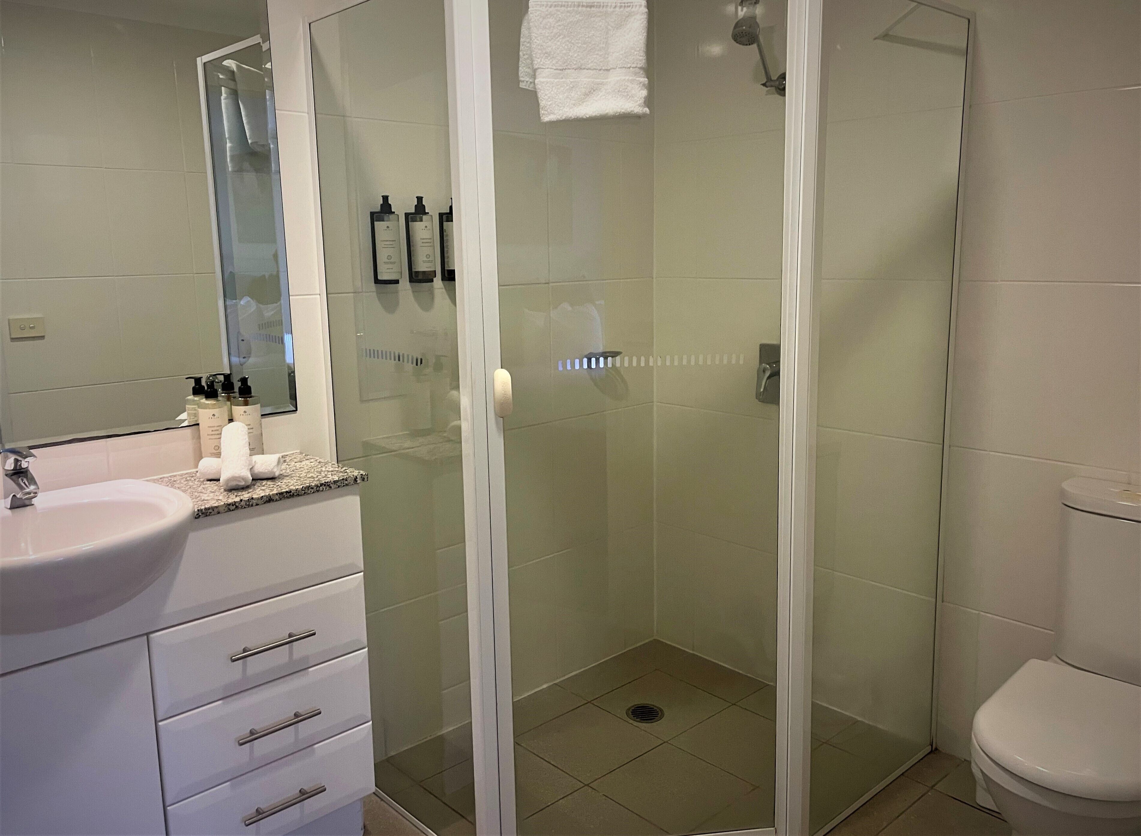 A modern bathroom with a glass-enclosed shower, a white sink, and a vanity with toiletries.