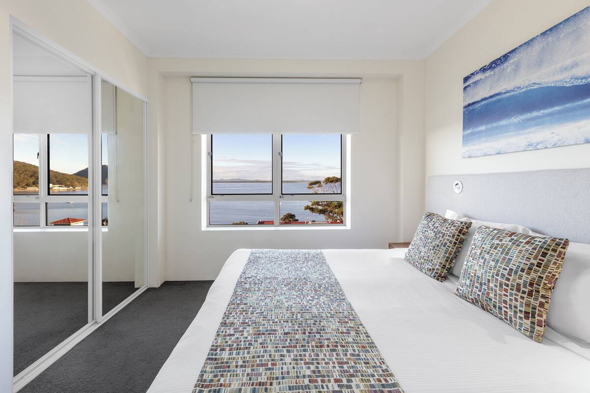 Ein Schlafzimmer mit einem großen Bett, Meerblick durch ein Fenster und einem Gemälde an der Wand.