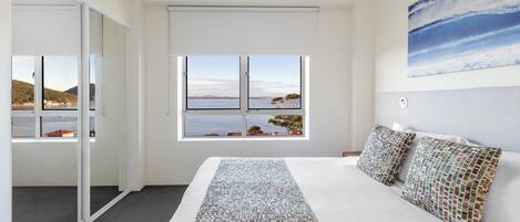 A bedroom with a large bed, a view of the sea through a window, and a painting on the wall.