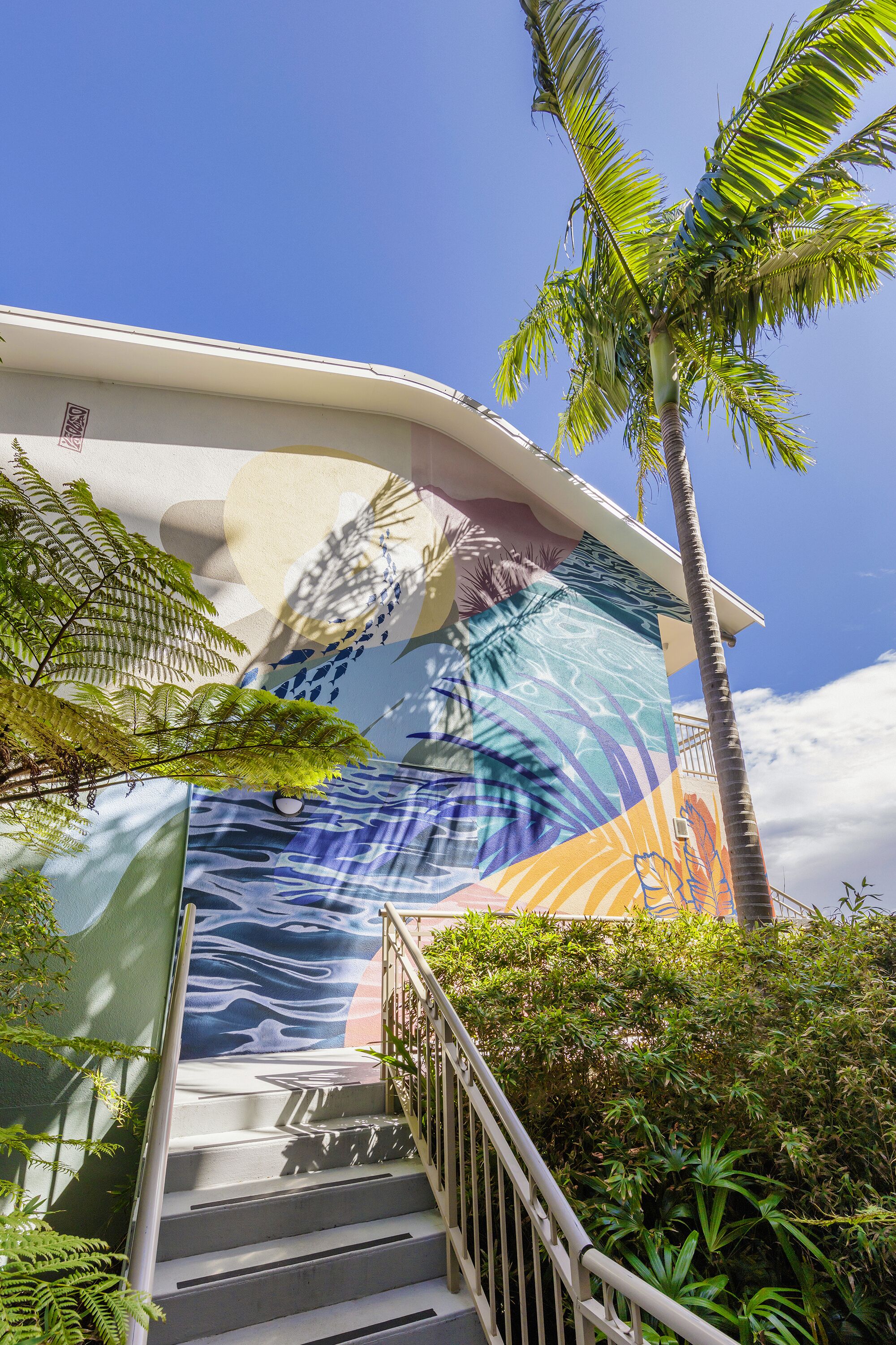 A staircase with a mural, palm trees, and greenery.
