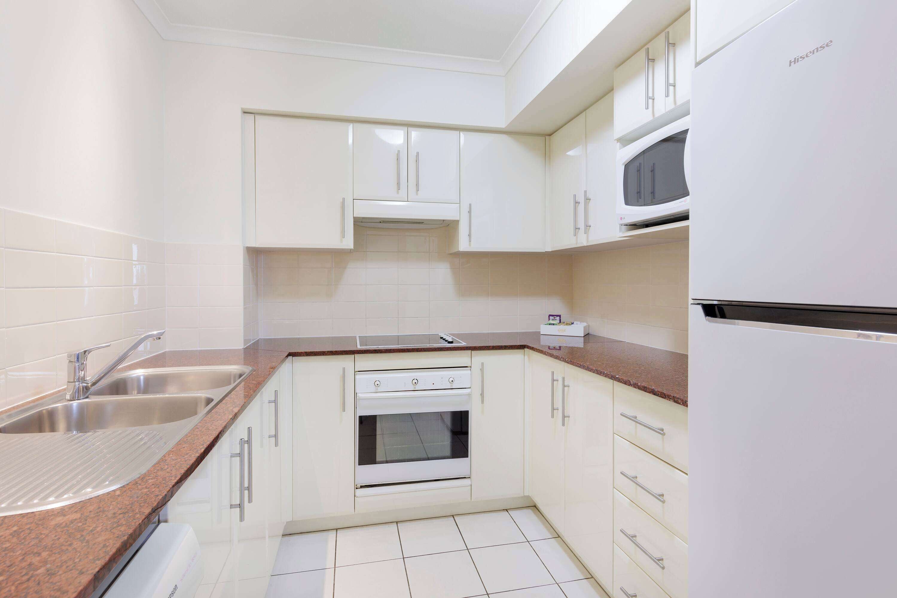 A kitchen with white cabinets, a stainless steel sink, a microwave, and a built-in oven.