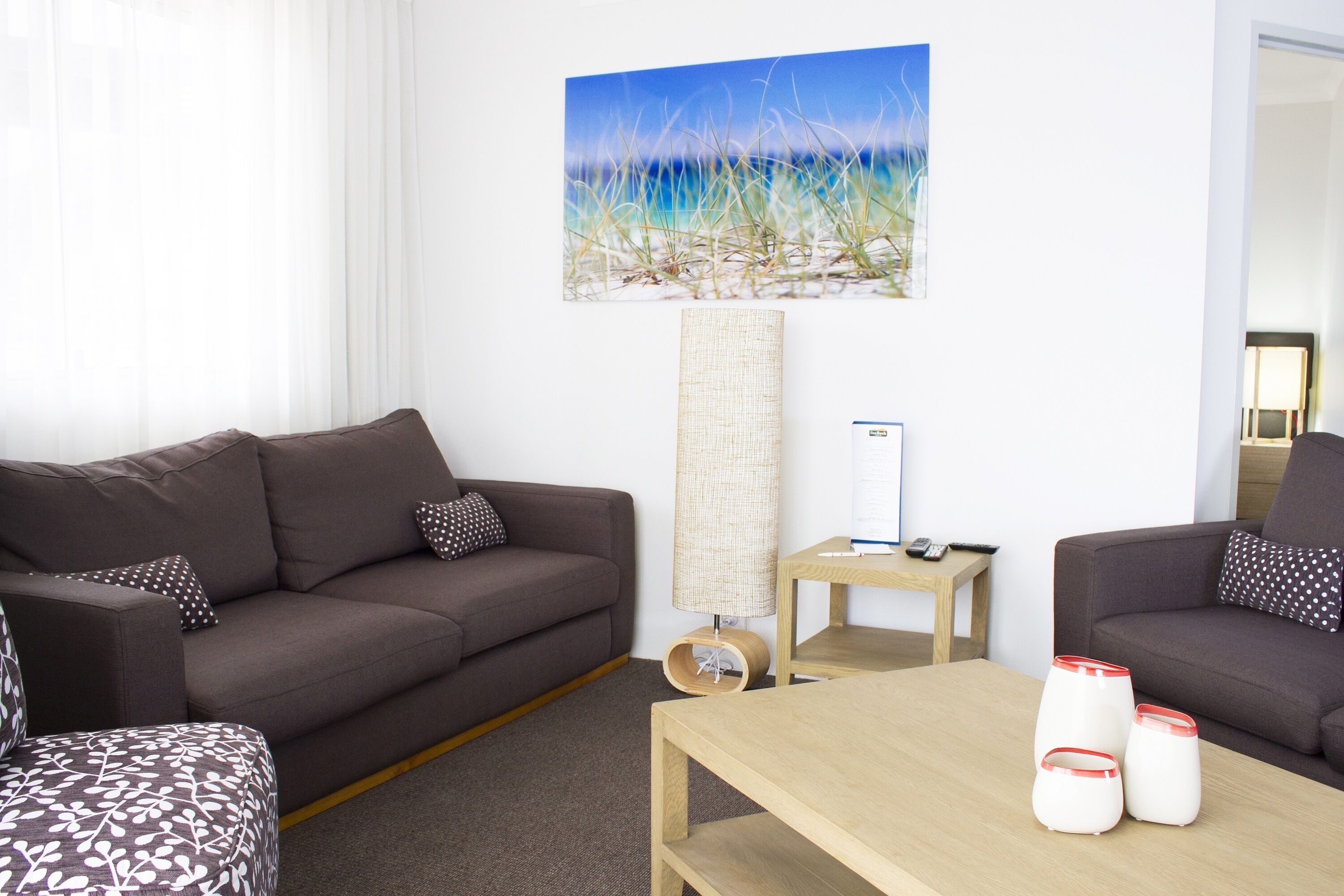 A modern living room with a brown sofa, a wooden coffee table, and a painting of a beach scene.