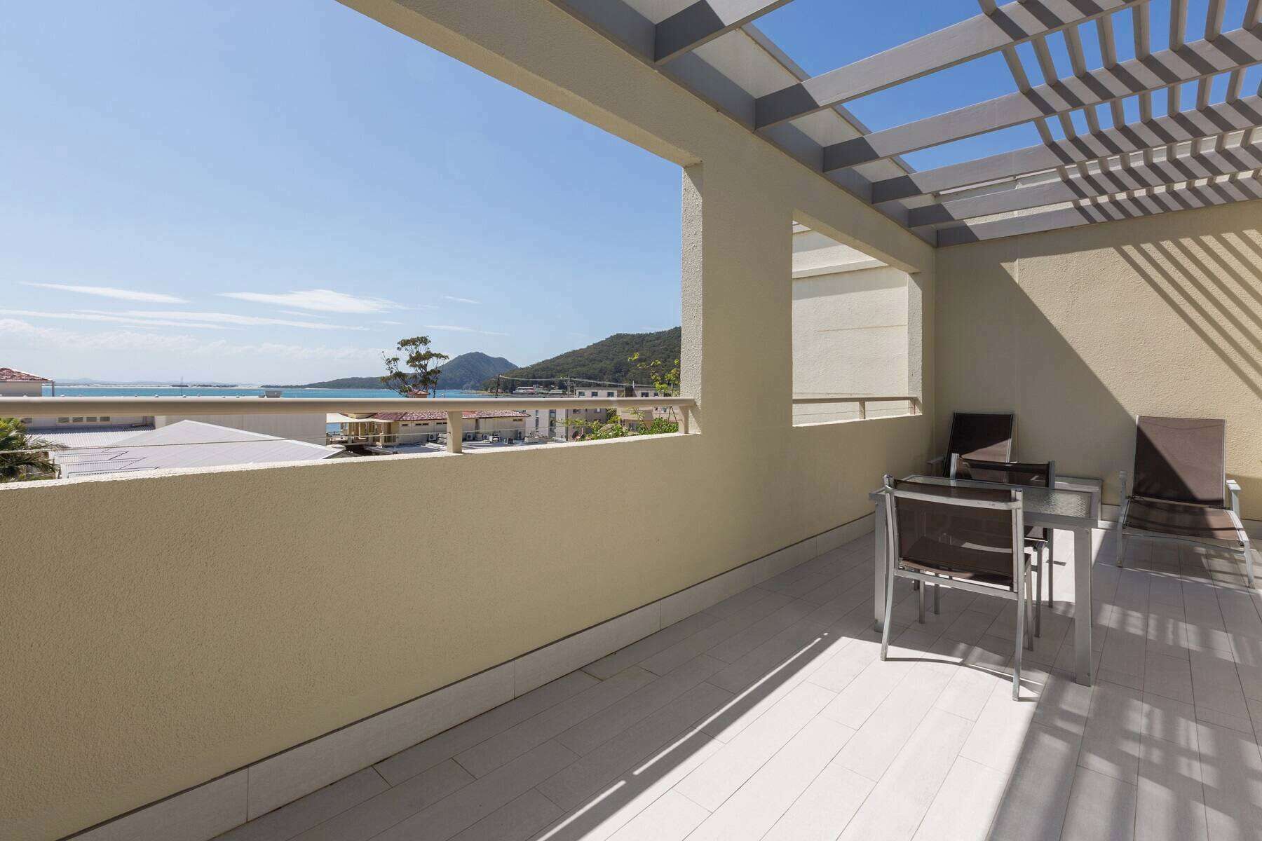 A balcony with a view of the sea and mountains, a pergola, and outdoor furniture.