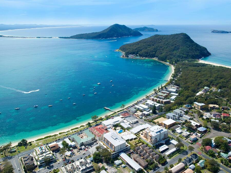 Vista aérea de un pueblo costero con playa, barcos y edificios residenciales.